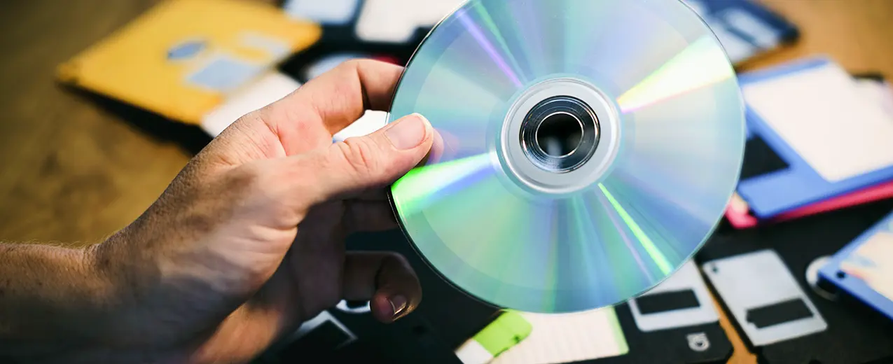 Hand holding CD with floppy disks in the background